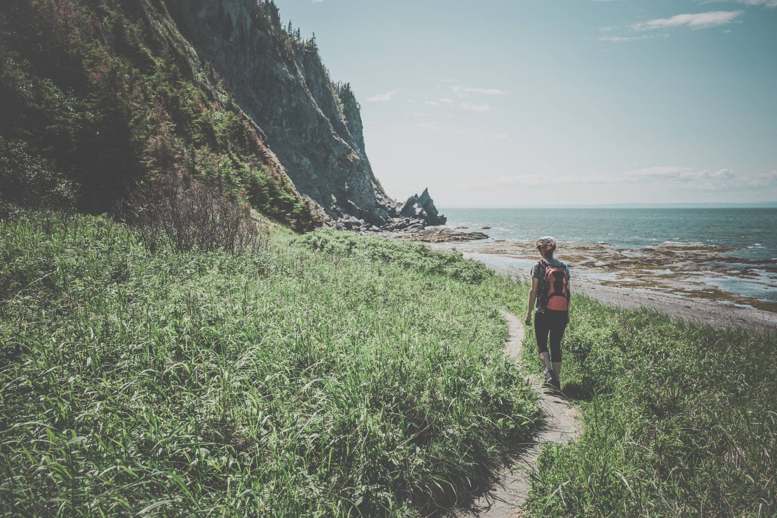 Une randonneuse sur un sentier au pied des falaises, au bord de la mer
